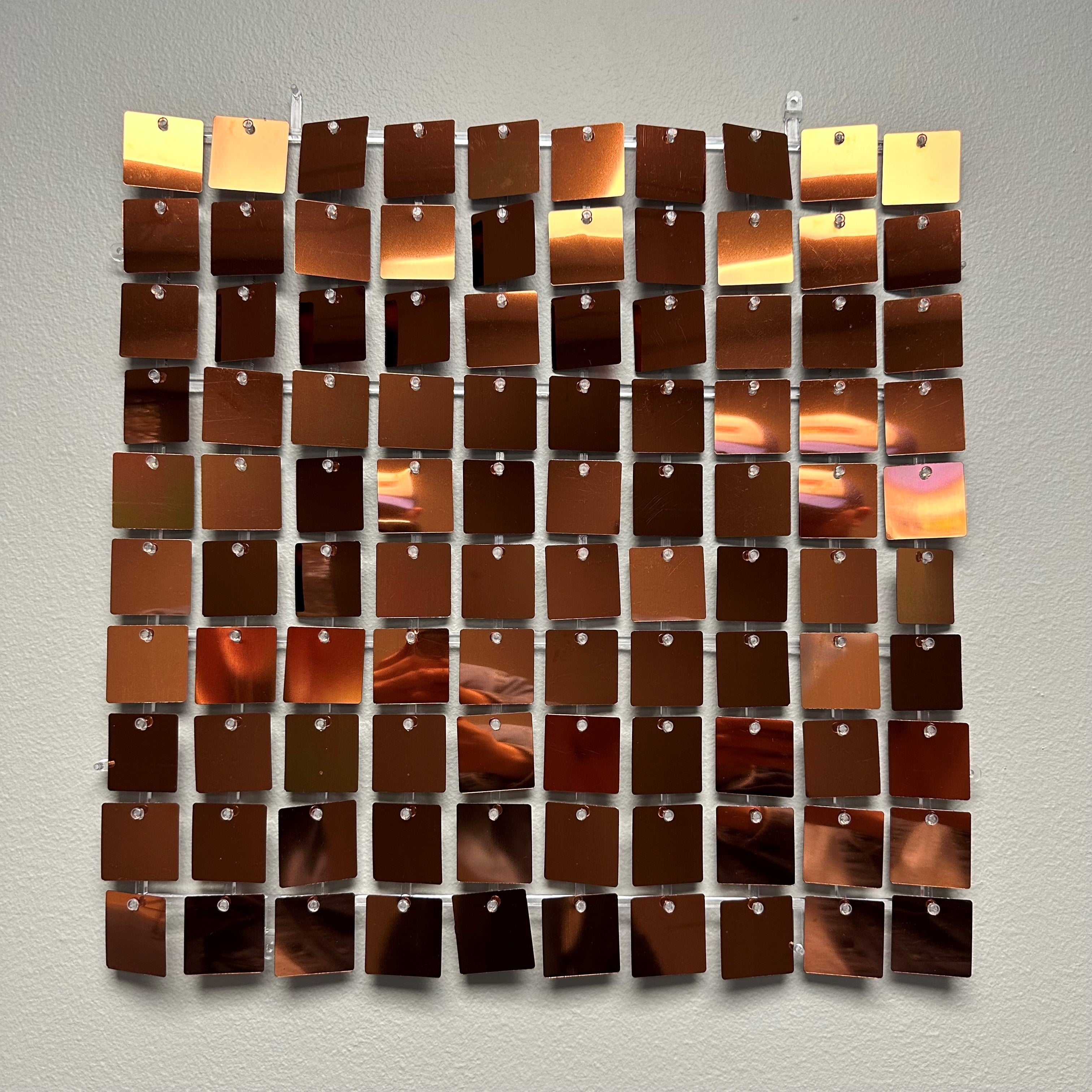 Glitrende veggplate med kvadratiske metallbiter i kobber og oransje toner