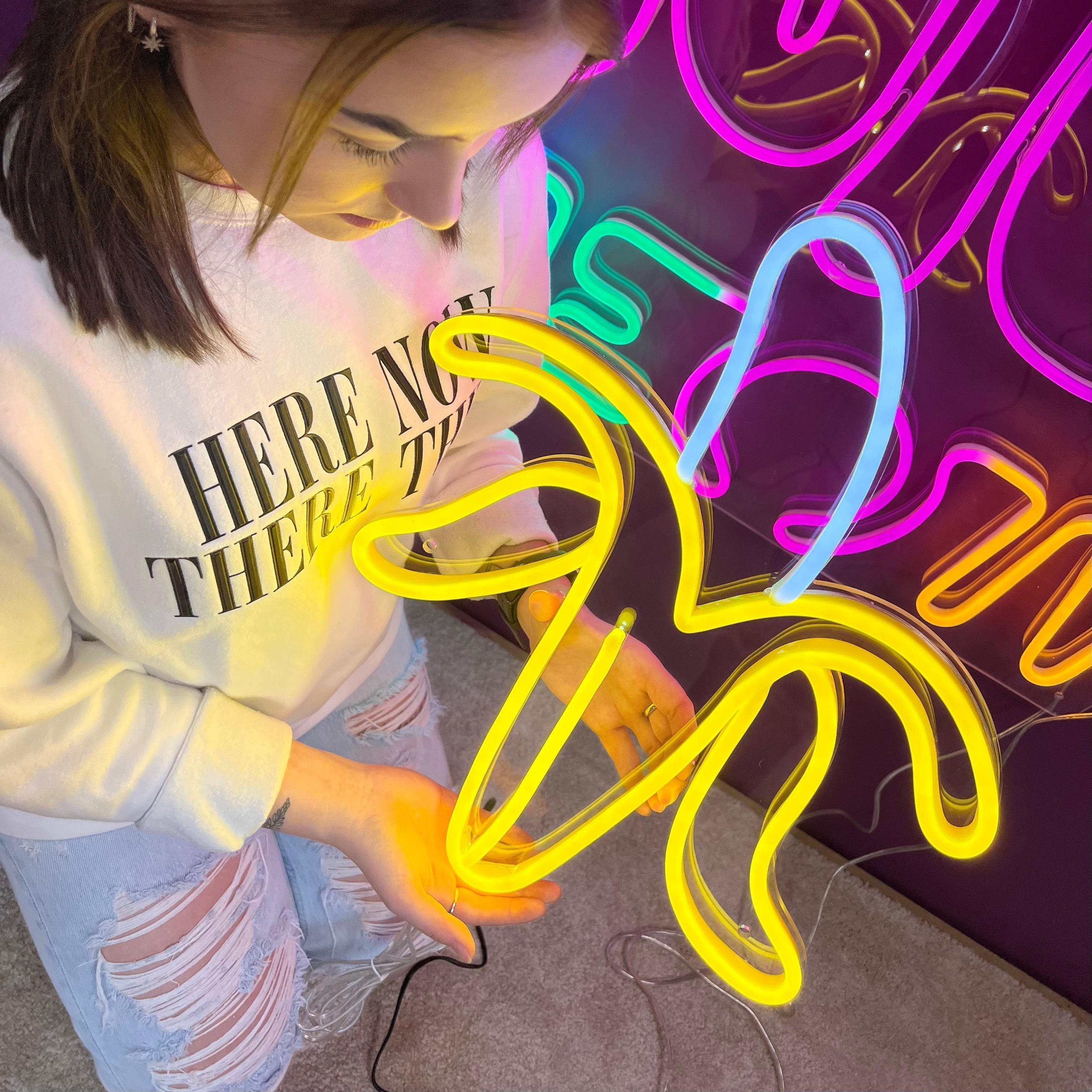 LED-neonskilt i bananform med gult og rosa flerfarget lys.