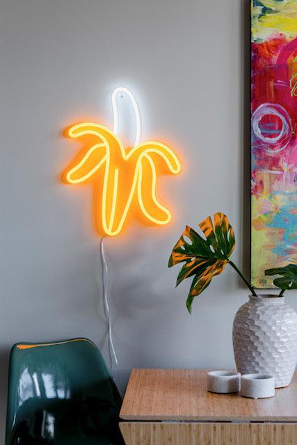 LED-neonskilt banan med gult neonlys og hvit kontur på stativ