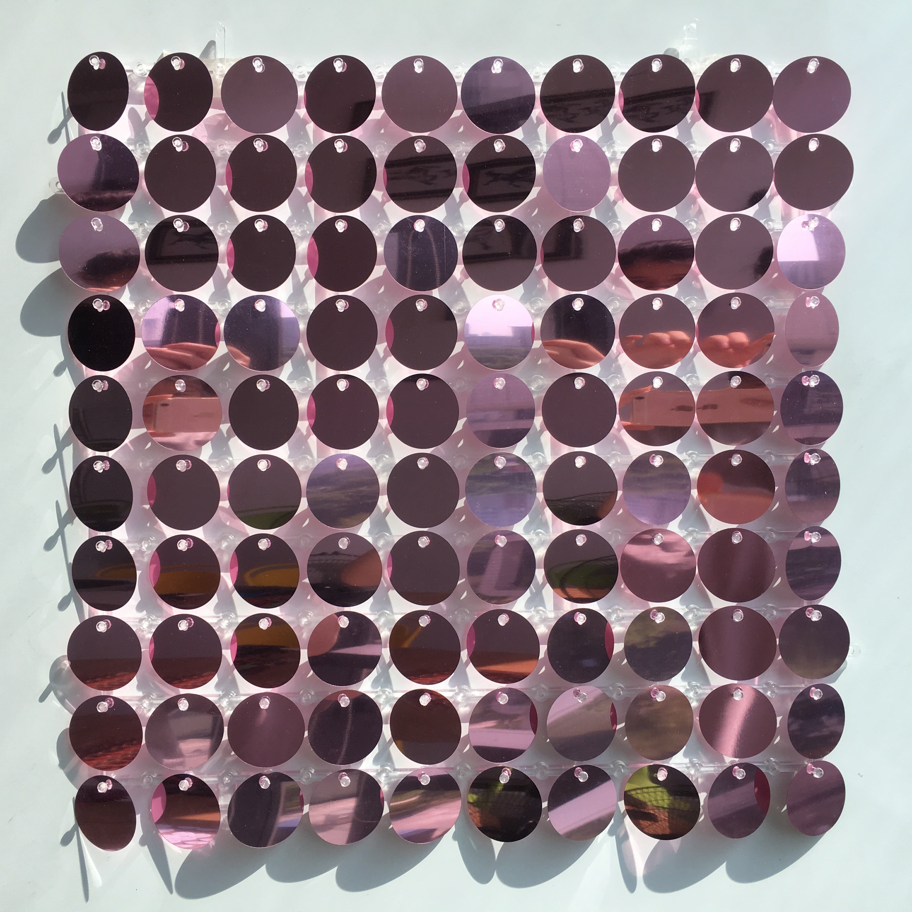 Glitrende veggplate med runde metallskiver i lilla og rosa toner, med festepunkter