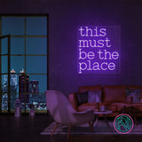 LED neonskilt med «this must be the place» i fiolett lys på vegg